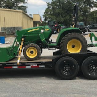 Green tractor secured on a black trailer, parked outdoors.