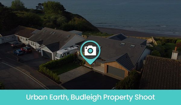 Aerial view of houses along a seaside road, with the ocean in the background. A camera icon is overlaid.