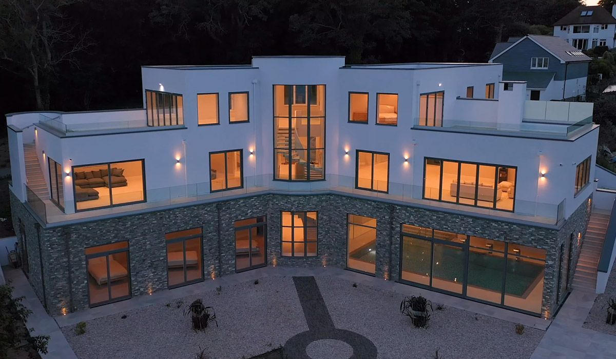 Modern white house with stone accents, illuminated windows at dusk.