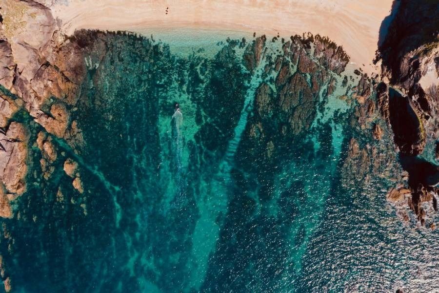 Aerial view of a turquoise ocean with rocky shoreline and a sandy beach.