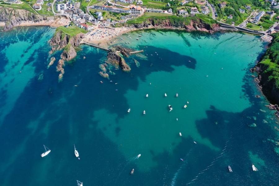 Aerial view of a turquoise cove with numerous boats, a sandy beach, and buildings along the shore.