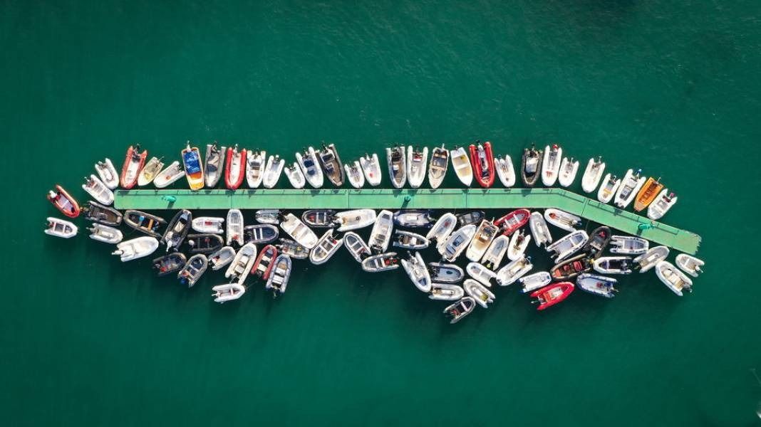 Aerial view of numerous small boats docked around a green pier in turquoise water.