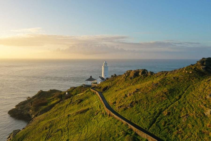 Lighthouse on a grassy cliff at sunset, overlooking the ocean.