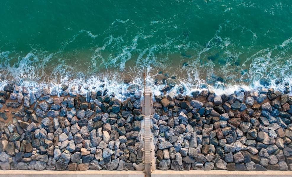 Stone breakwater against teal water, with a concrete pathway leading into the ocean.