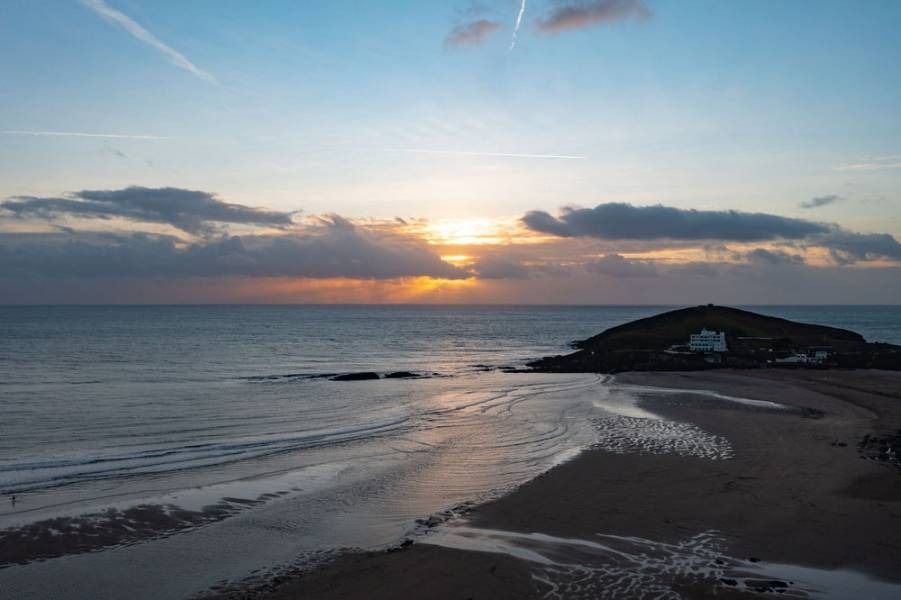 Beach at sunset with water, clouds, and island with a white building.