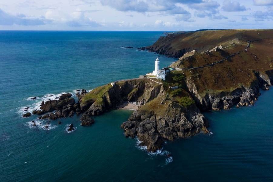 Lighthouse on a rocky cliff overlooking turquoise ocean under a partly cloudy sky.