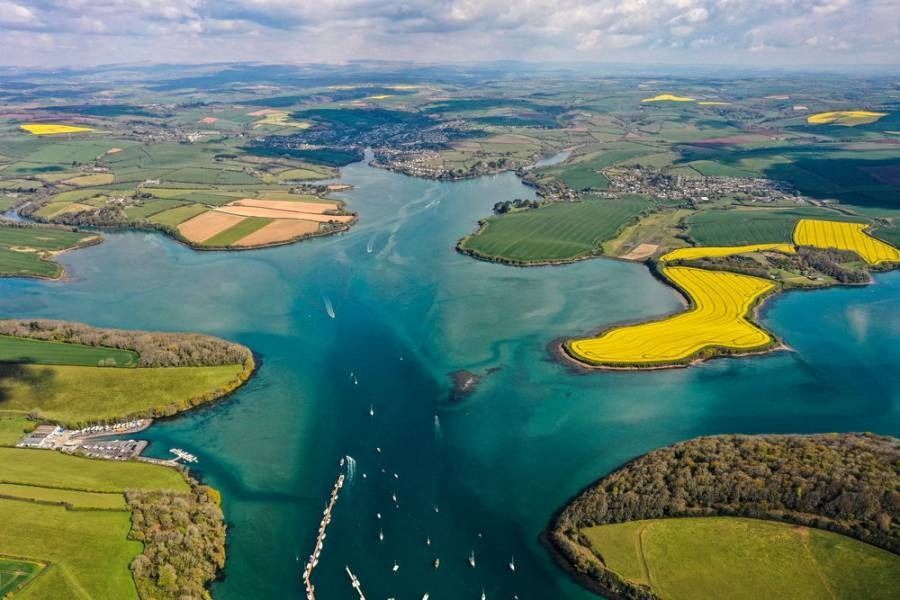 Aerial view of turquoise water, green fields, and yellow flowers, with boats sailing.