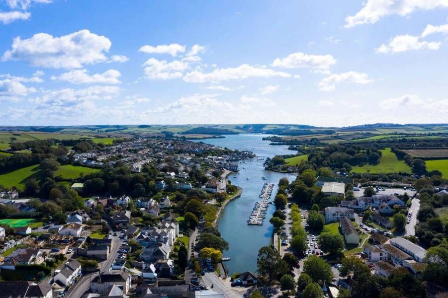Aerial view of a coastal town and harbor with boats on a sunny day. Green fields and blue sky.