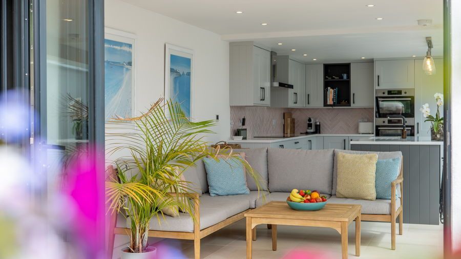 Lounge area opens to kitchen.  Light wood sofa with blue and yellow pillows, small table with fruit.
