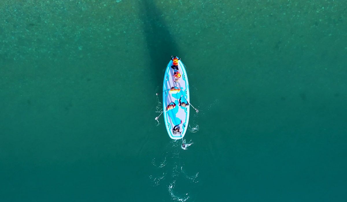 Kayak with three people paddling on turquoise water. Overhead view.