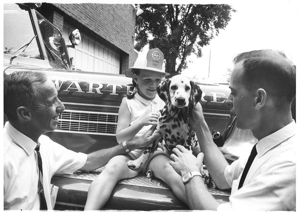 A girl in an honorary chief’s helmet holds a Dalmatian puppy with two members.