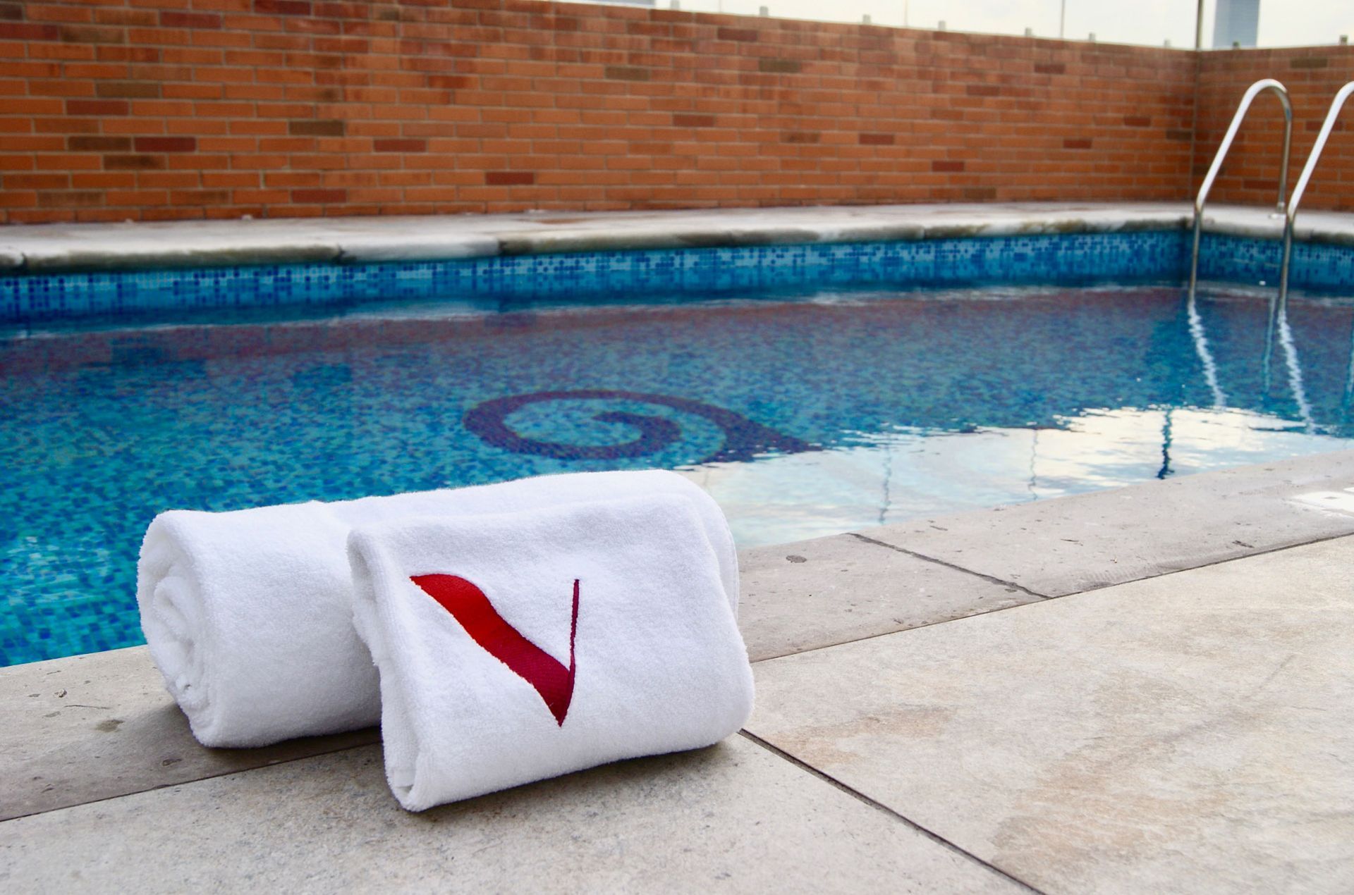 Toallas blancas enrolladas junto a una piscina de agua azul y una escalera de metal.