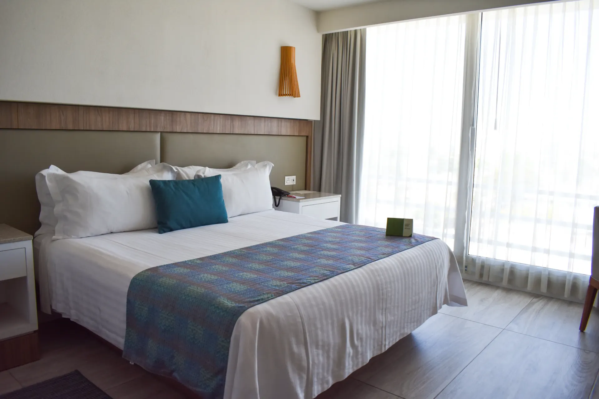 Habitación luminosa con cama de matrimonio, detalles en azul y grandes ventanas con cortinas transparentes.