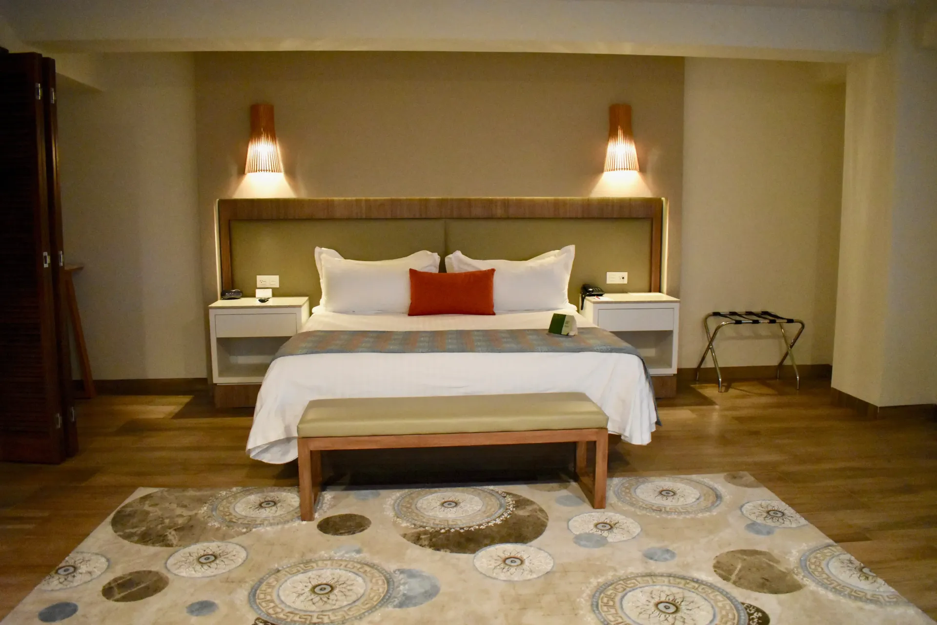 Elegante dormitorio con cama blanca, iluminación cálida y alfombra estampada.