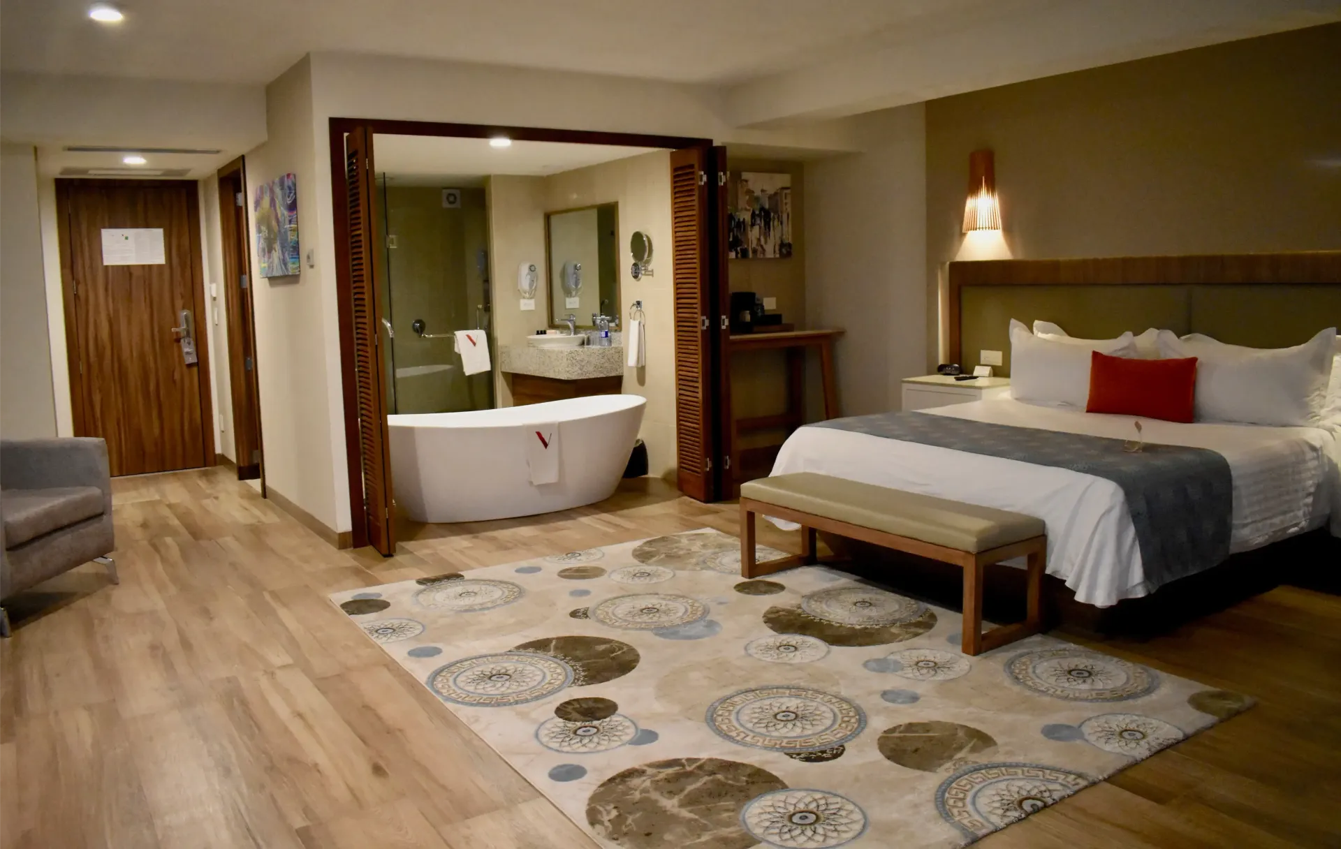 Habitación de hotel con cama king size, zona de estar y baño abierto con bañera grande.