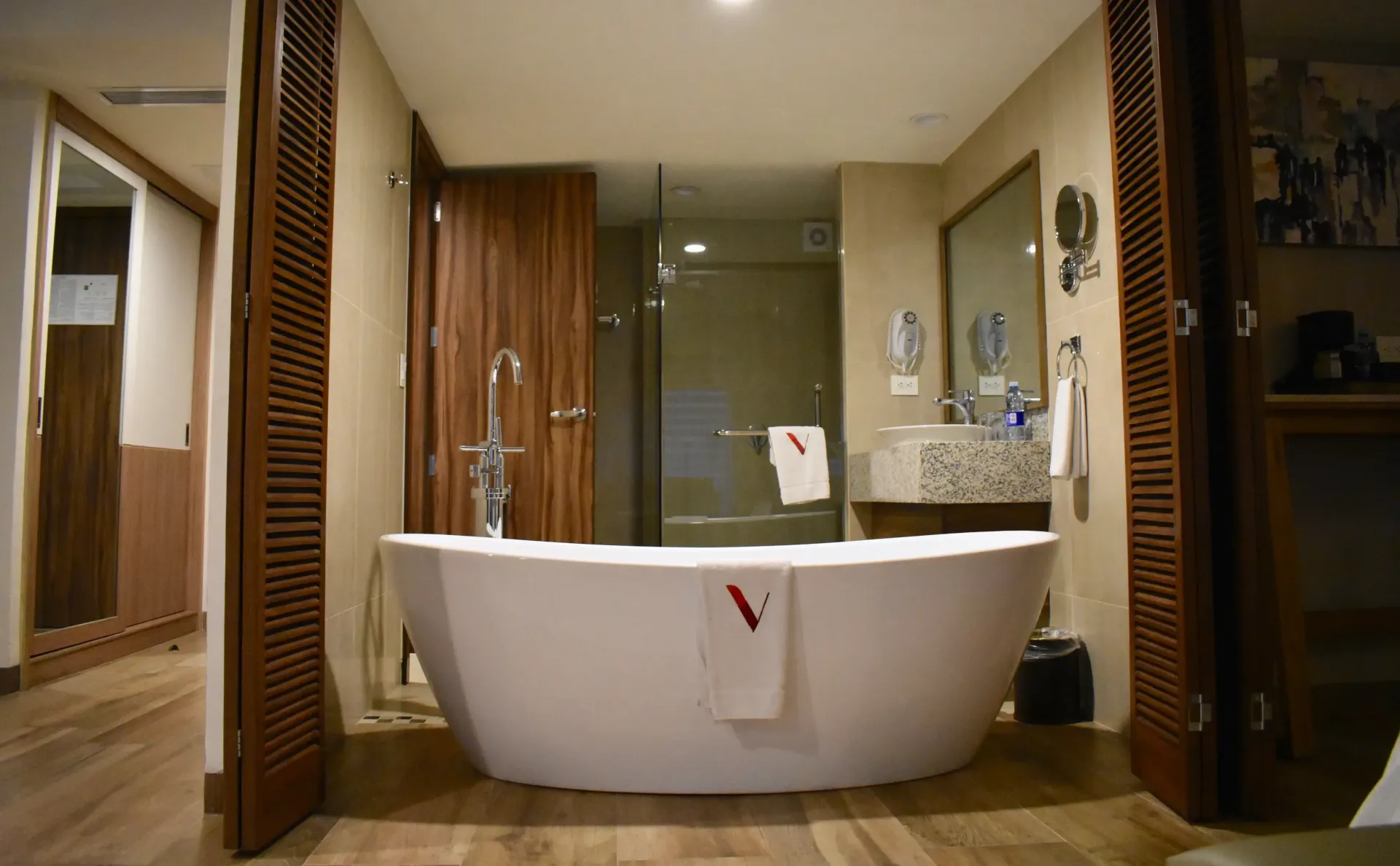 Baño moderno con bañera blanca independiente, lavabos dobles y detalles en madera cálida.
