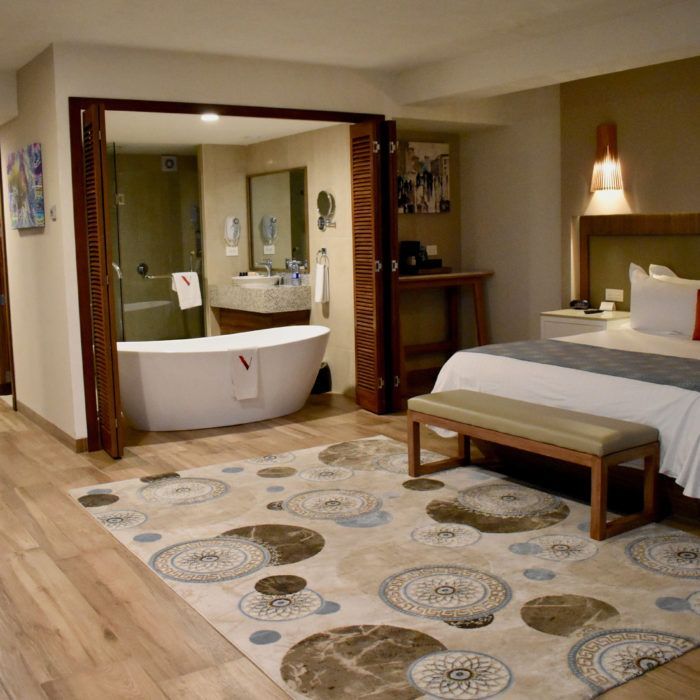 Dormitorio espacioso con baño abierto, alfombra estampada, cama y suelo de madera.