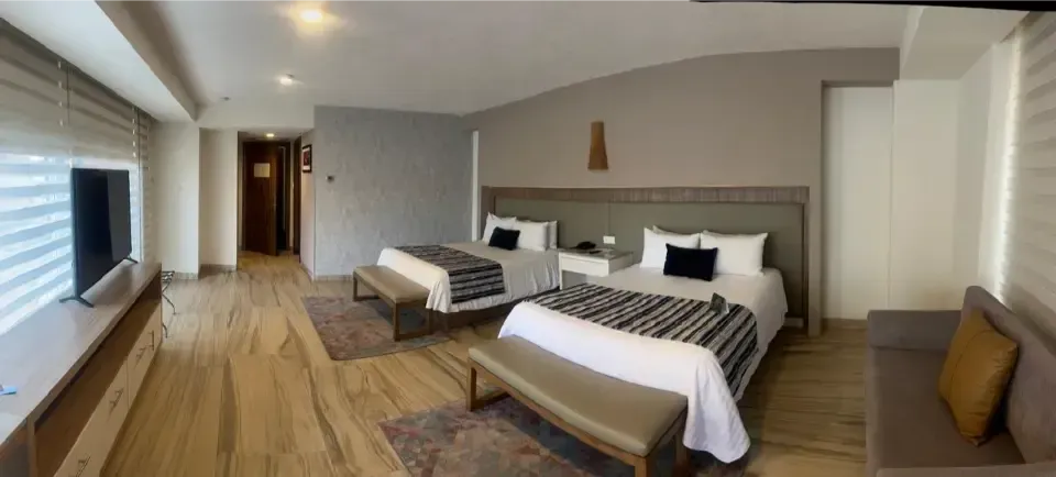 Habitación de hotel moderna con dos camas, suelo de madera, persianas y zona de estar.