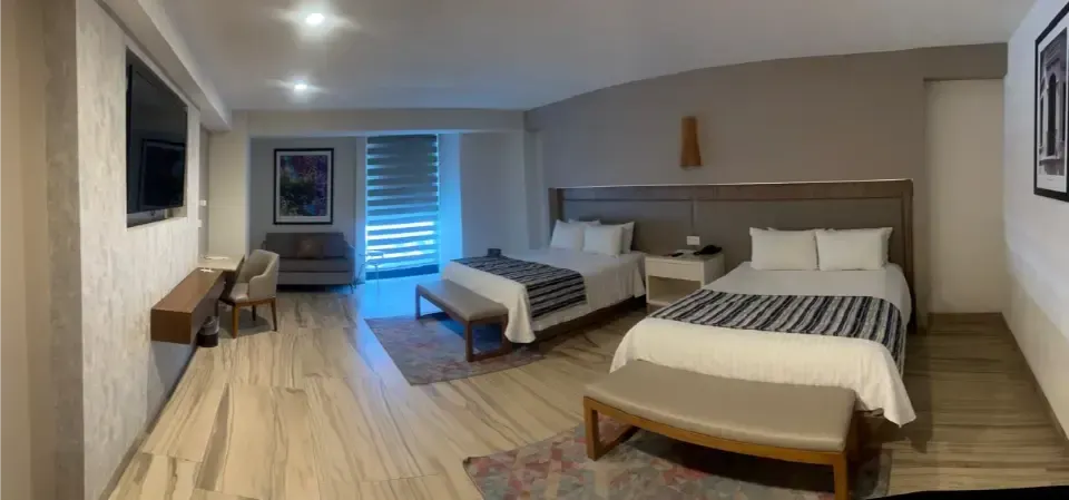 Habitación espaciosa con dos camas, suelo de madera, cómoda y persianas cerca de la puerta.