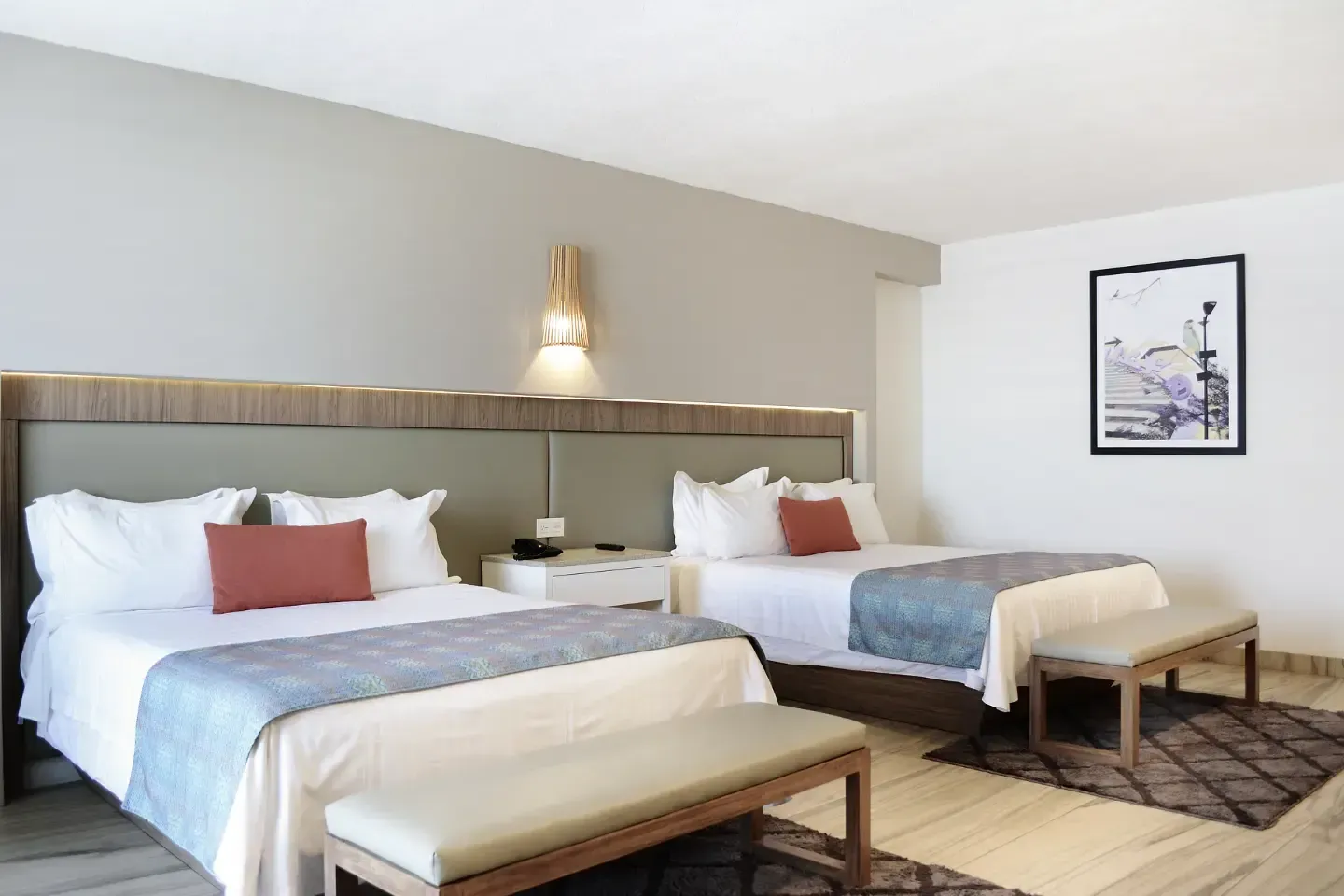 Habitación de hotel con dos camas bien hechas, ropa de cama azul y una lámpara de pared.