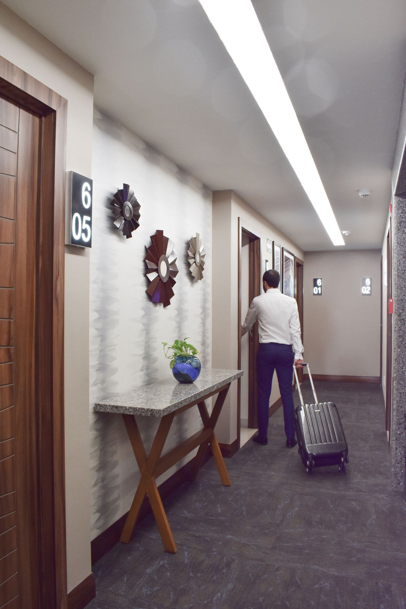 Una persona empuja una maleta por el pasillo de un hotel, pasando por delante de las puertas de las habitaciones.