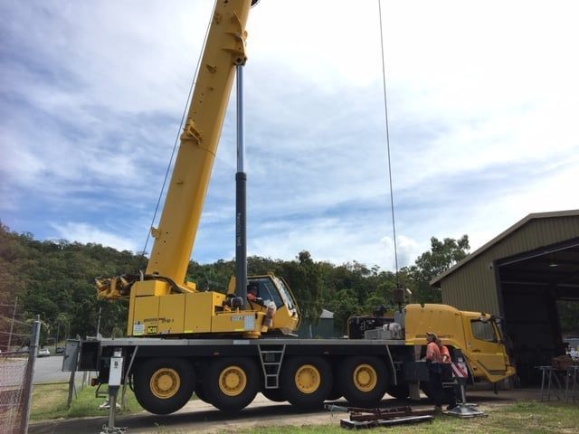 A large yellow crane is parked in front of a building — Kelly's Crane Hire in Mossman, QLD