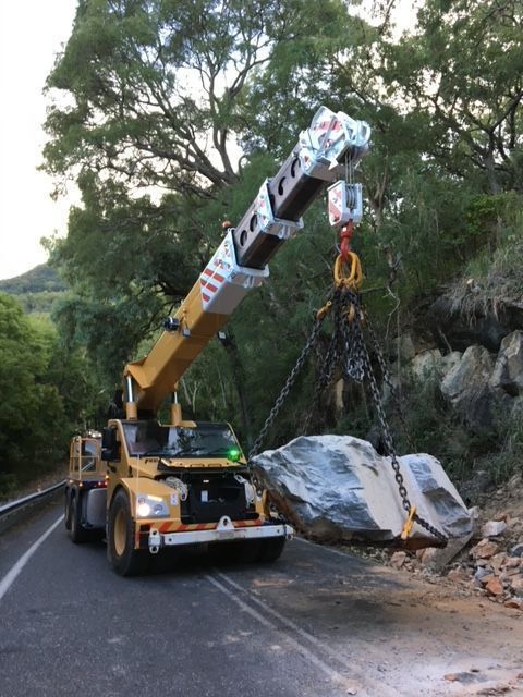 A Crane is Lifting a Large Rock Down a Road — Kelly's Crane Hire in Mossman, QLD