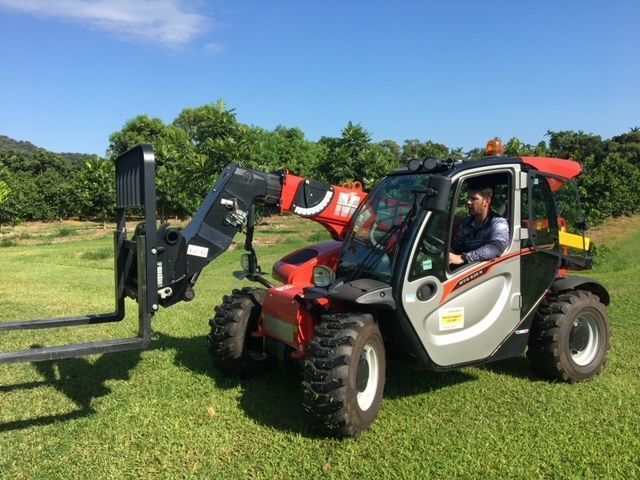 A Man is Driving a Forklift in a Grassy Field — Kelly's Crane Hire in Mossman, QLD