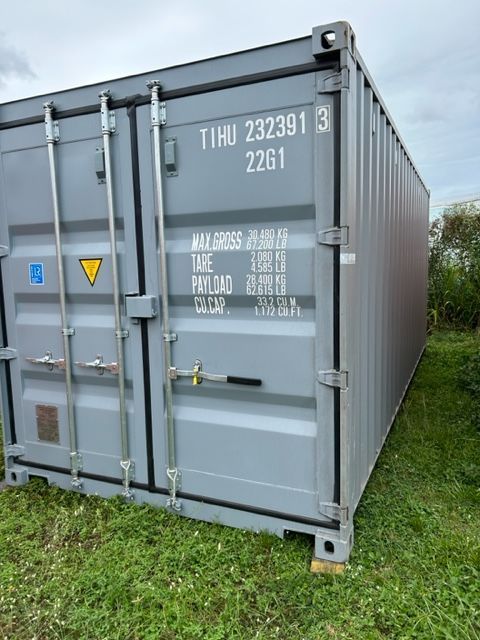 A Gray Shipping Container is Sitting on Top of a Lush Green Field — Kelly's Crane Hire in Mossman, QLD