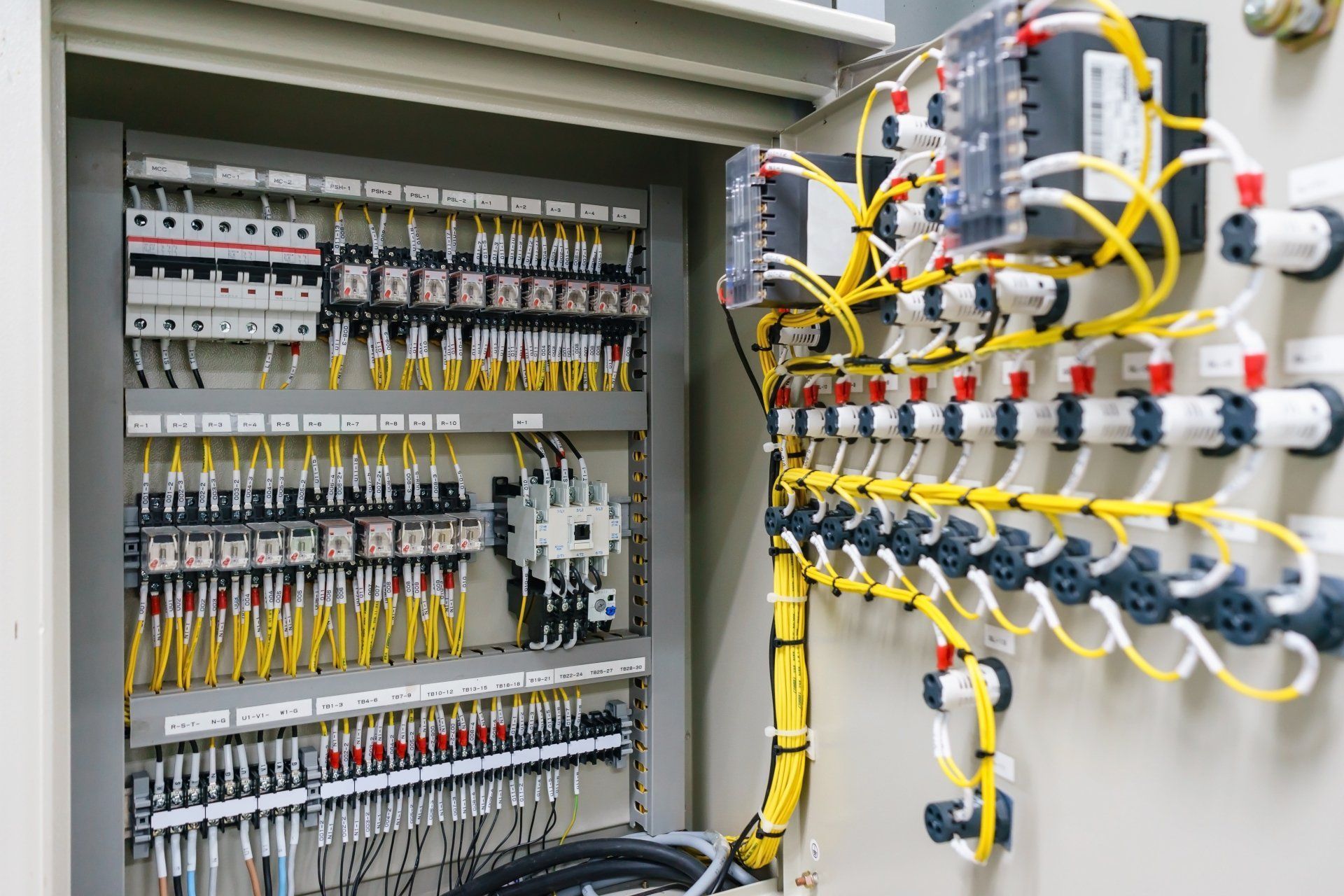 An open electrical control panel featuring rows of terminal blocks, relays, and neatly organized yellow and white wiring.
