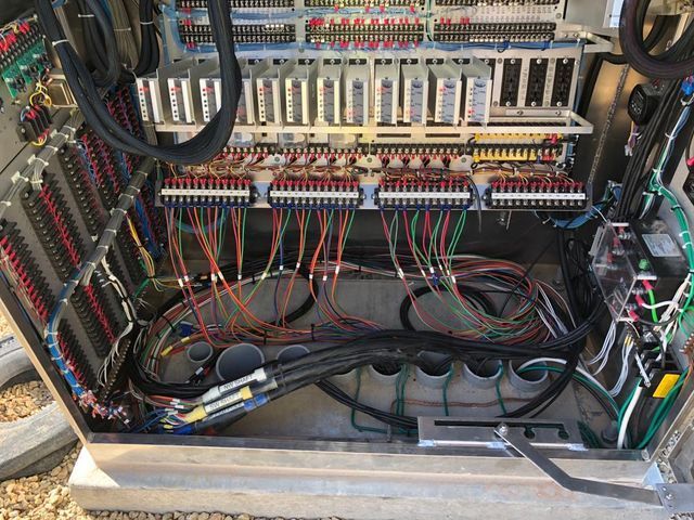 An open industrial electrical control cabinet filled with various relays, terminal blocks, and complex wiring.