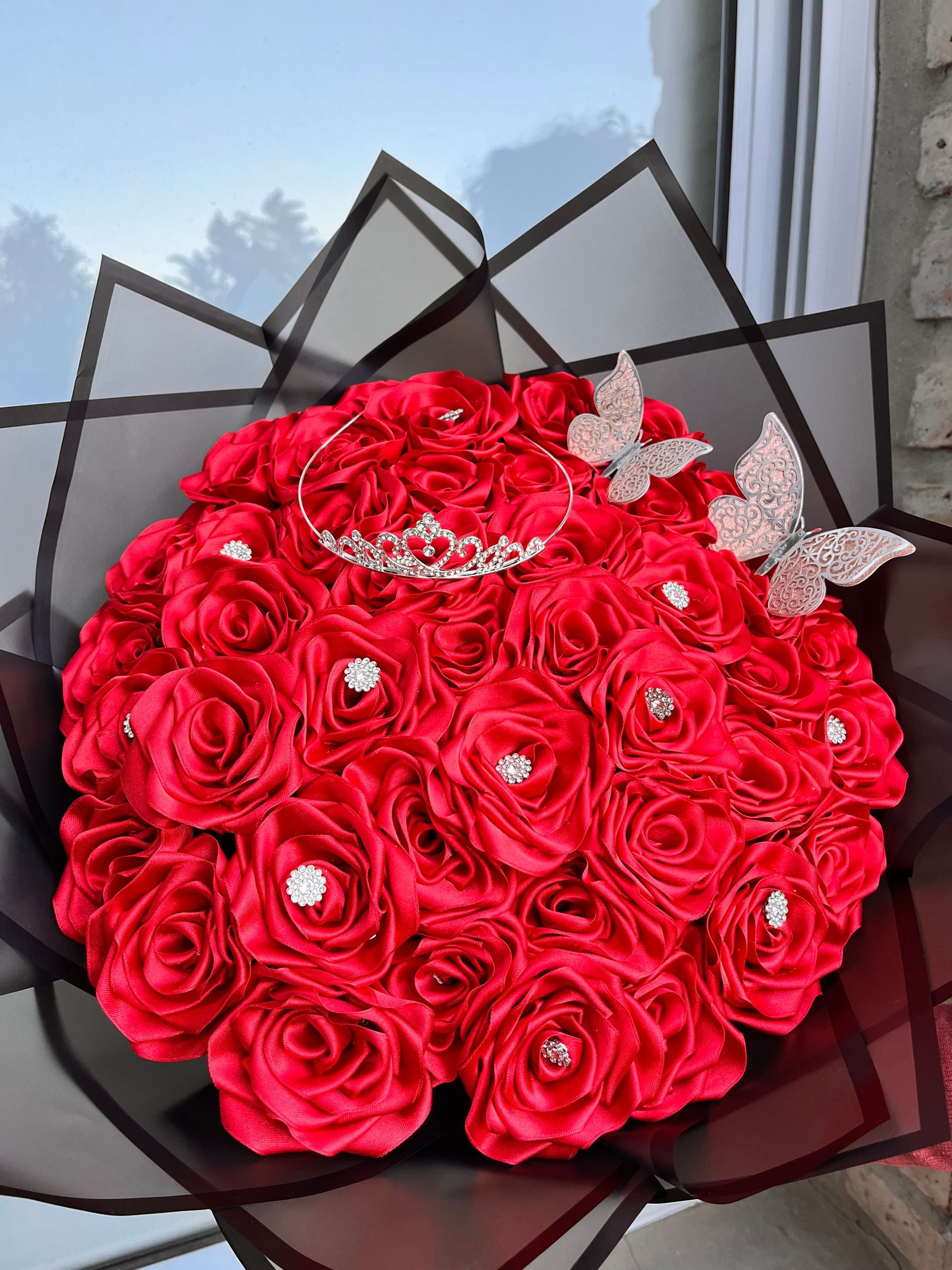 Ramo de rosas rojas brillantes envuelto en papel negro junto a una ventana.