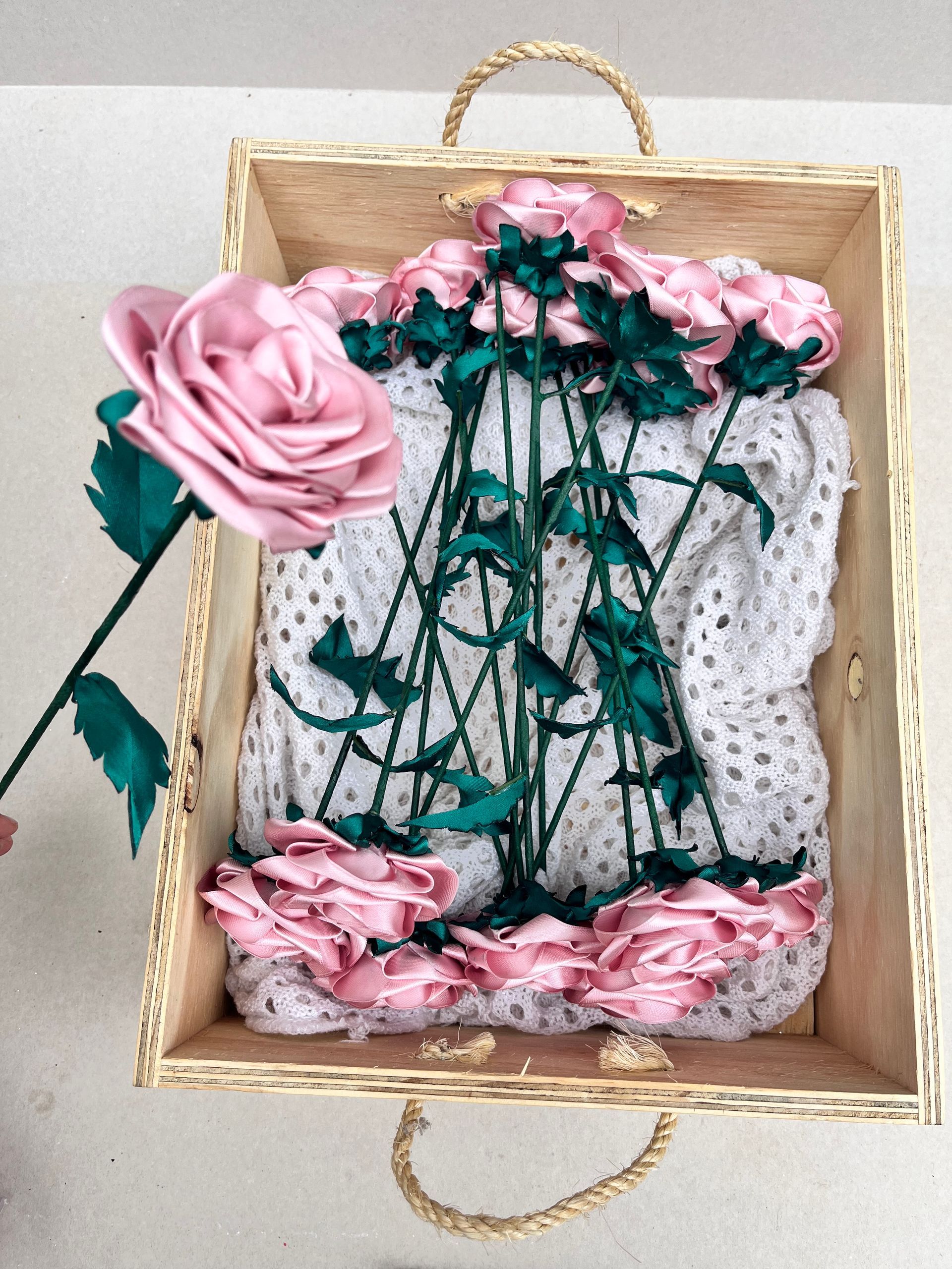 Una mano sostiene un ramo de rosas rosadas apoyado contra el tronco de un árbol con hojas turquesas.