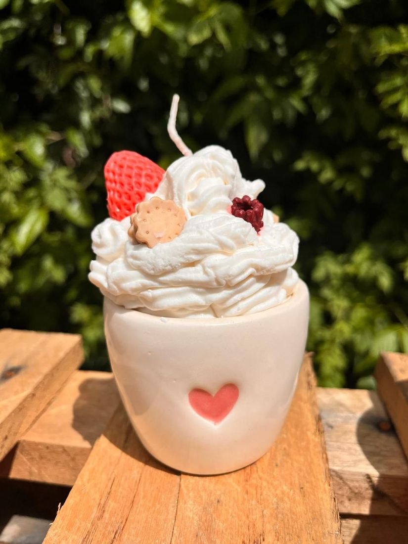 Taza blanca cubierta con crema batida y fresas sobre una superficie de madera al aire libre.