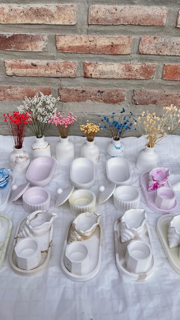 Exhibición de zapatillas blancas sobre una tela blanca, con decoraciones florales y un fondo de pared de ladrillos.