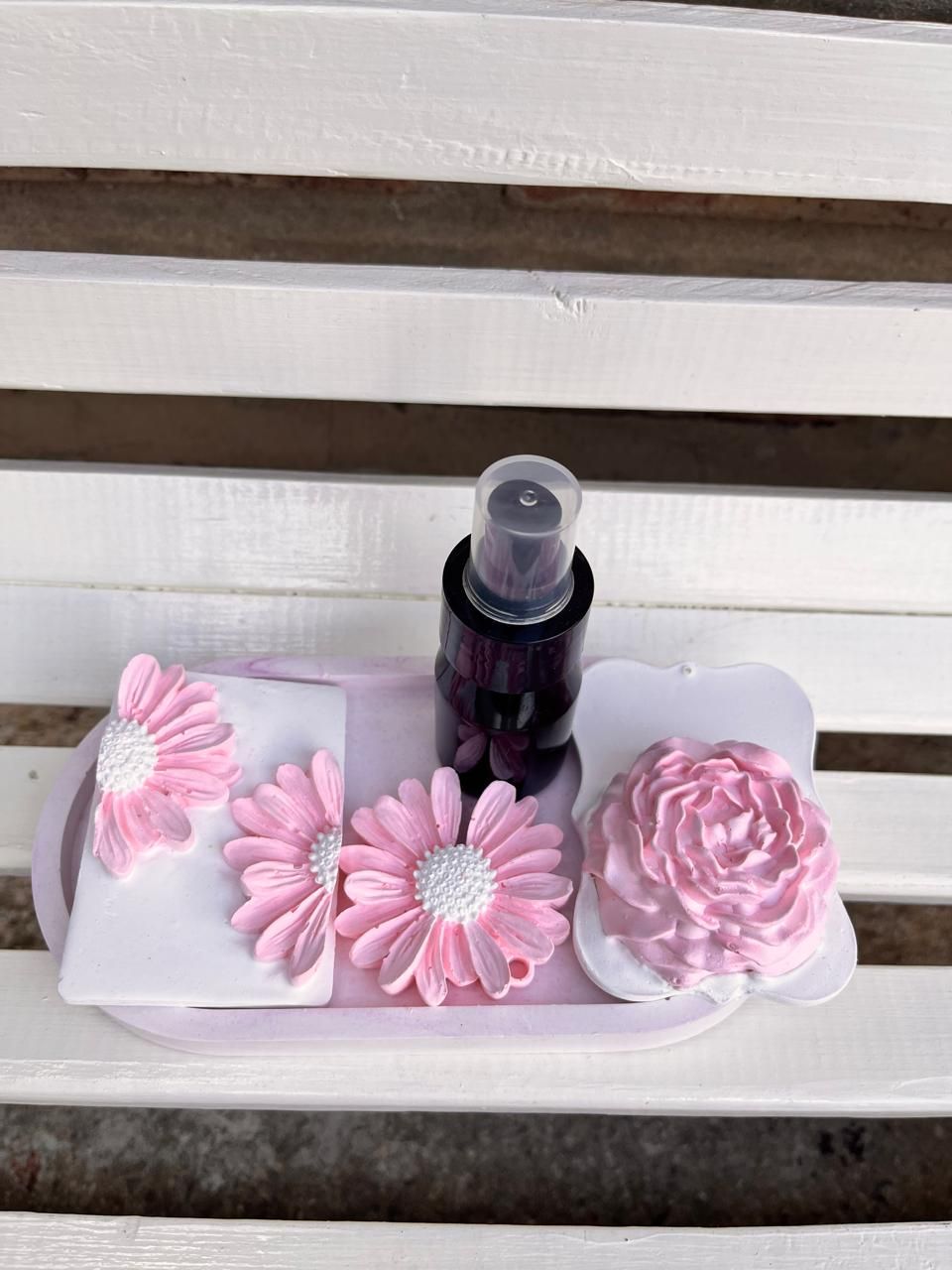 Expositor de jabón con forma de flor rosa con una pequeña botella oscura sobre una bandeja blanca.