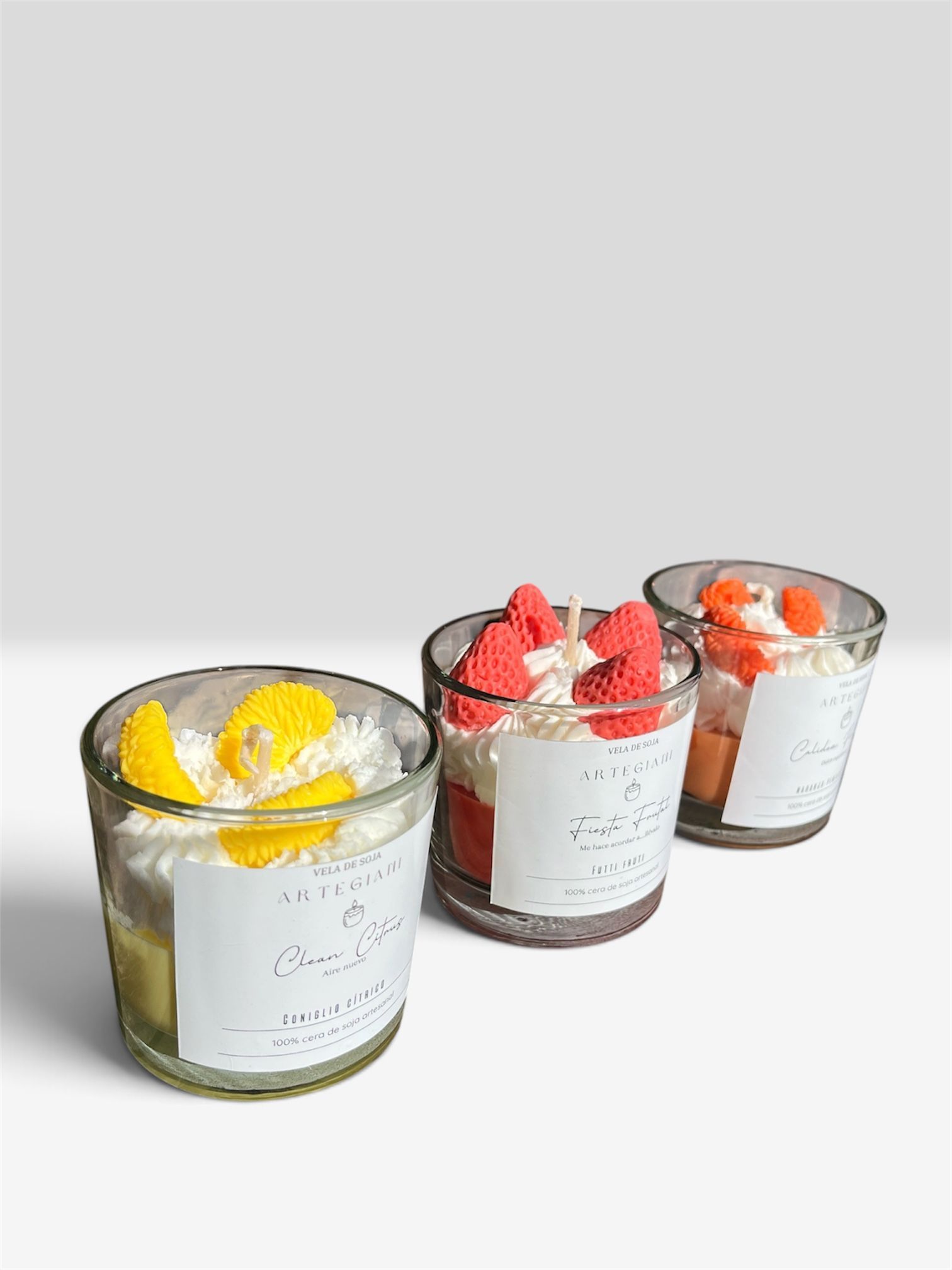 Tres copas de postre de cristal con capas de mousse y cobertura de frutas sobre una superficie blanca.