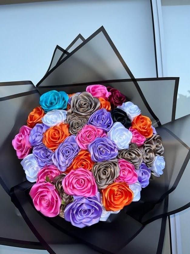 Ramo de rosas multicolores envuelto en papel negro sobre un fondo claro.