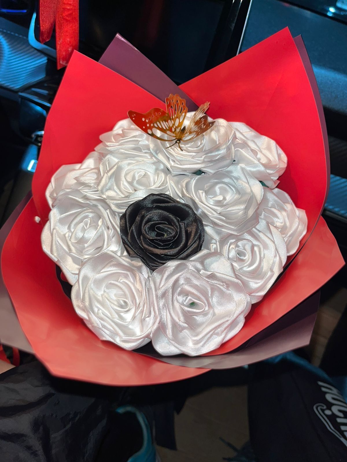 Ramo de rosas blancas con centro negro y envoltorio rojo, rematado con un pequeño lazo dorado.