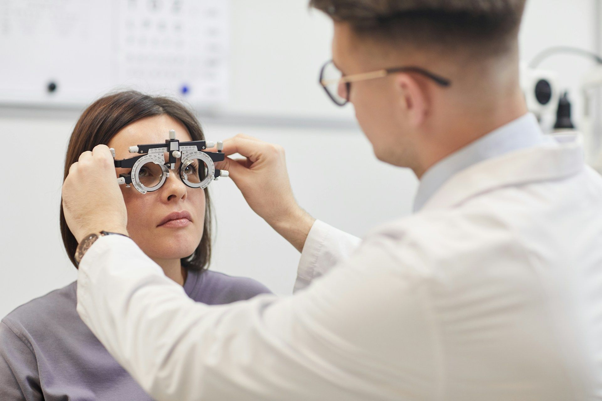 Optometrist adjusting a trial frame on a patient in an eye exam room.