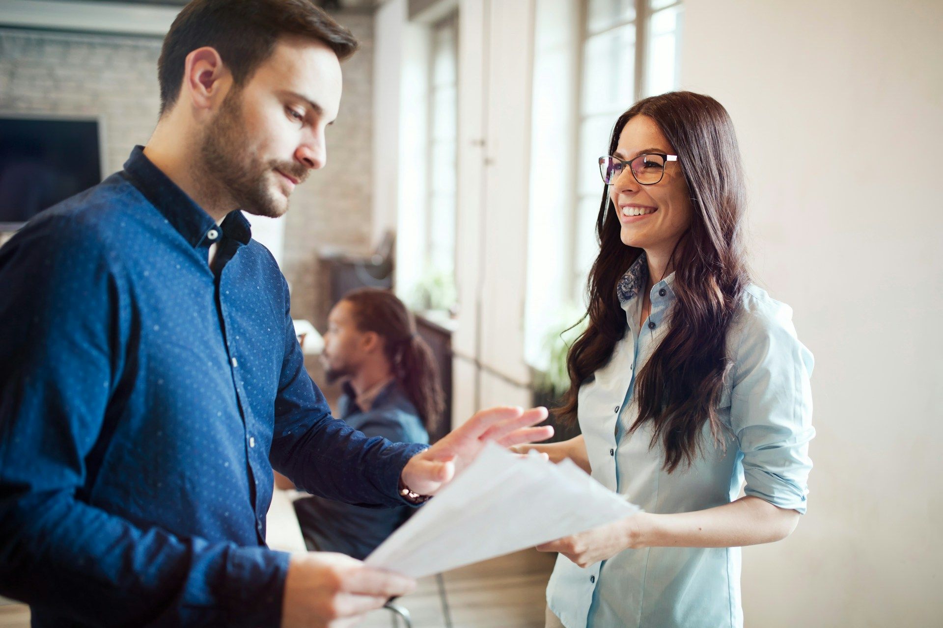 Man and woman reviewing papers, smiling in an office setting.