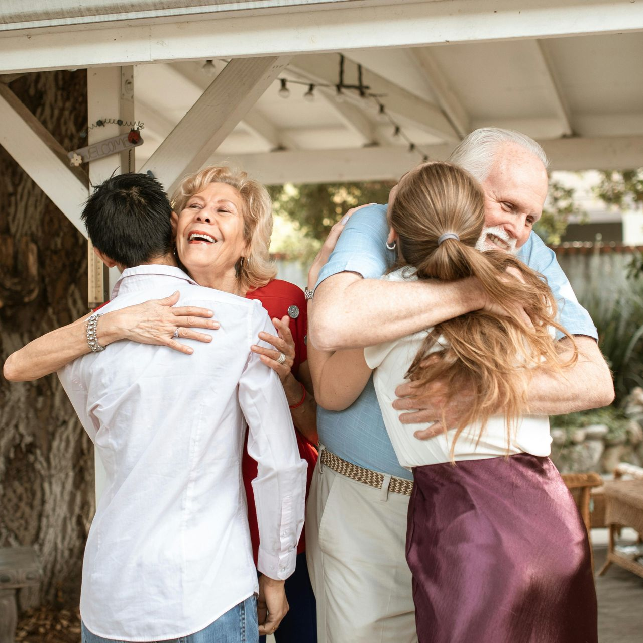 Elderly couple embracing two young people outside; happy smiles.