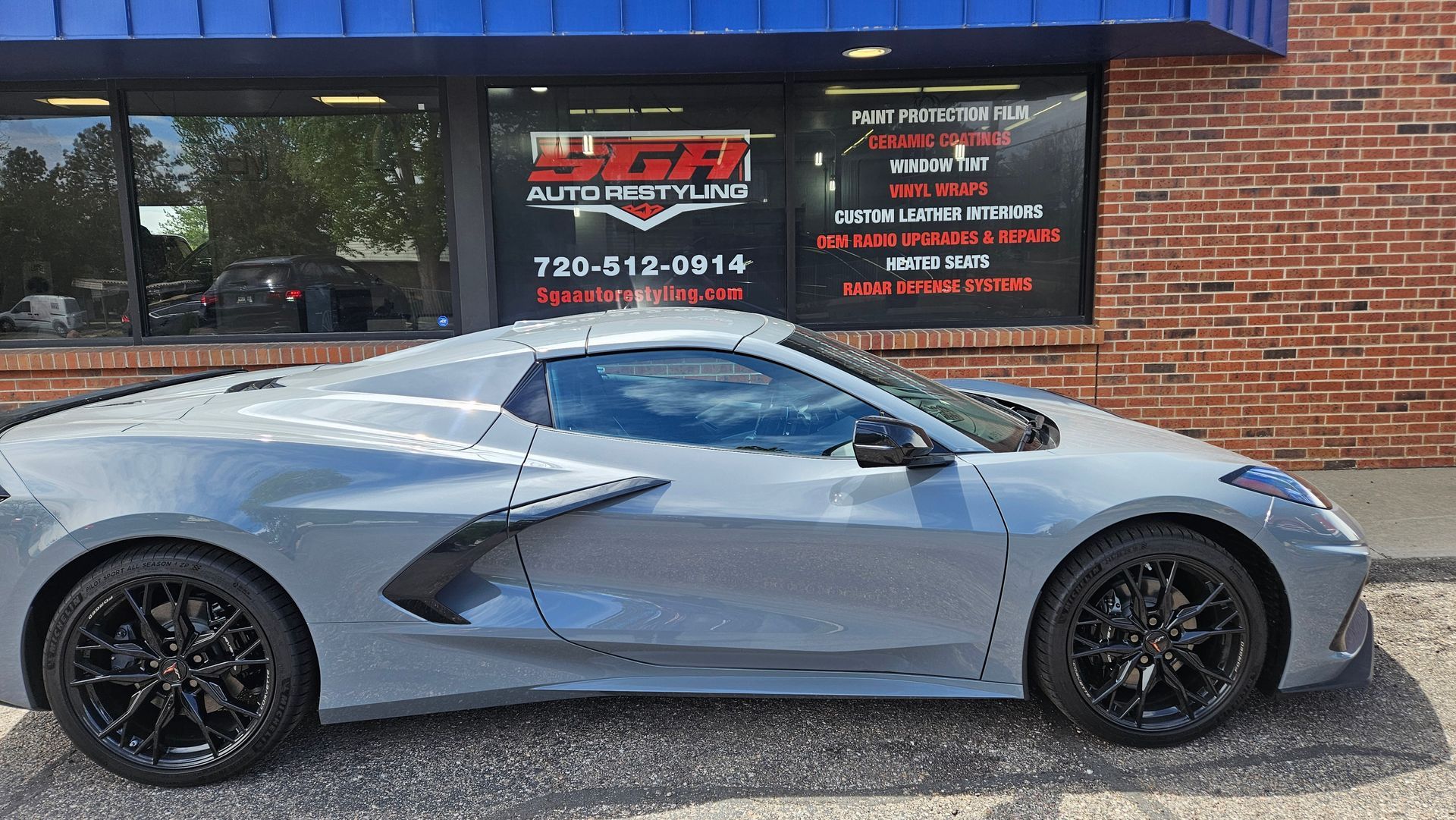 Gray sports car parked in front of a storefront with a business sign, black wheels.