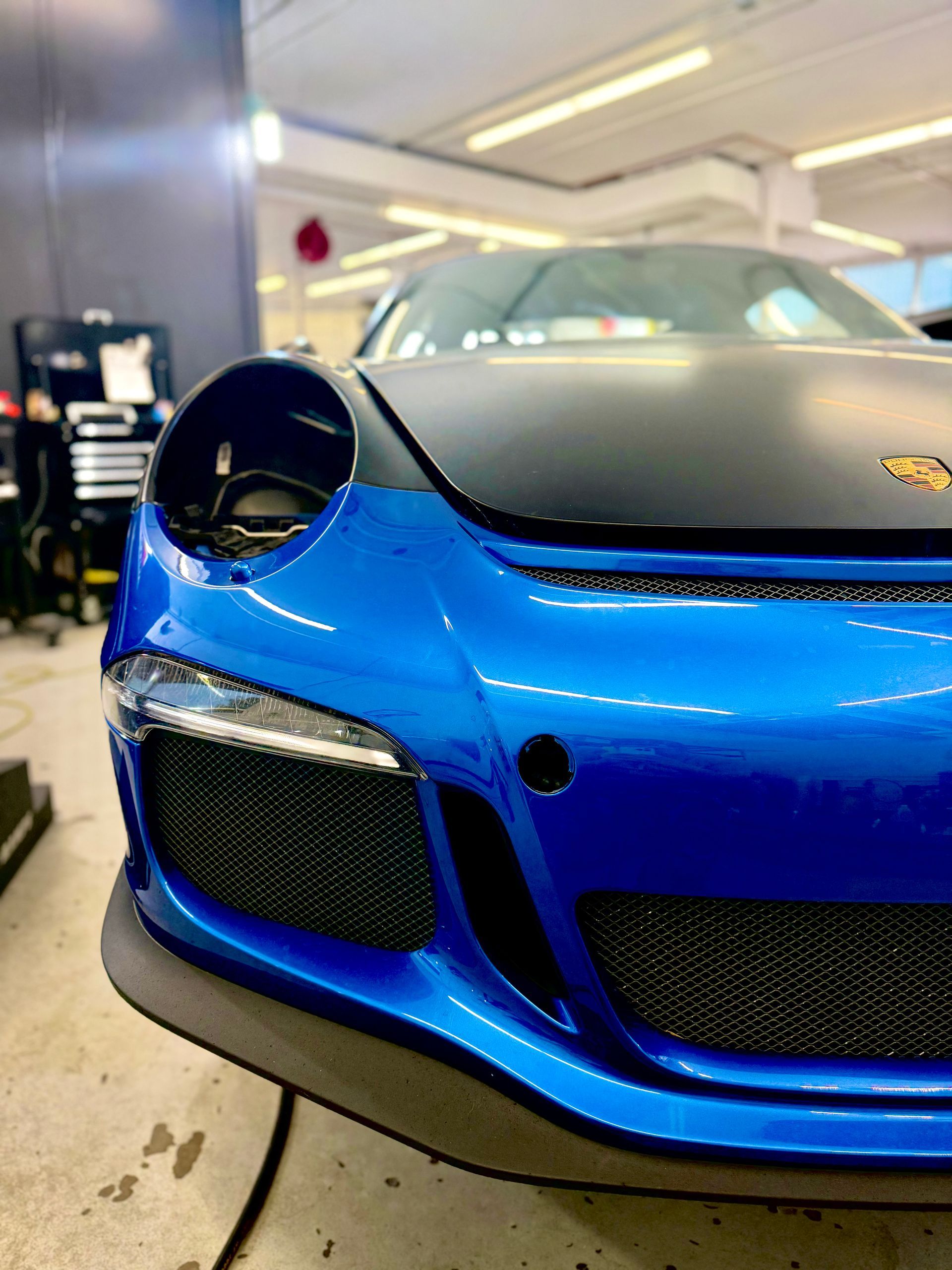 Blue and black Porsche sports car in a garage, partially obscured by the camera angle.