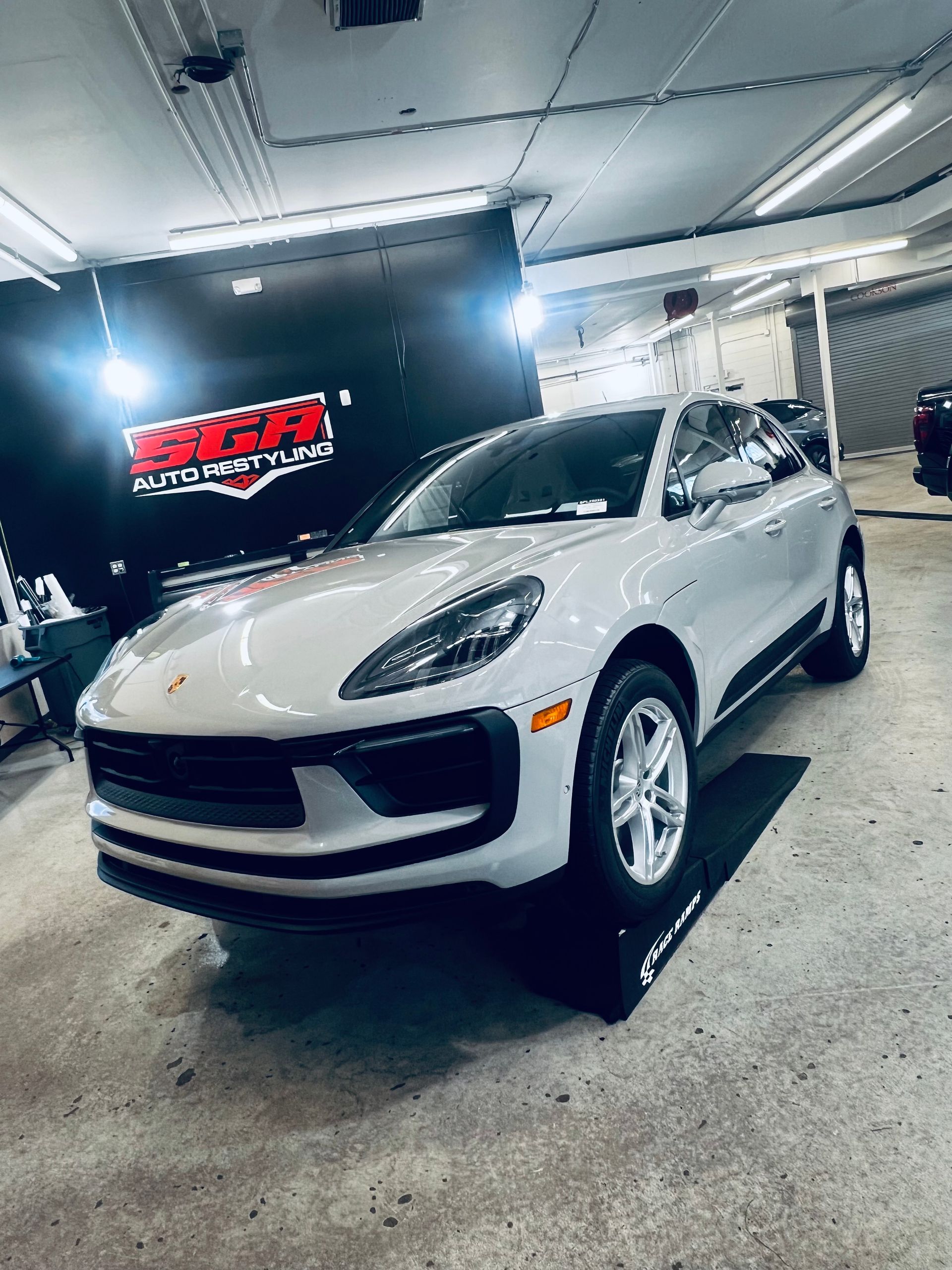 White Porsche Macan SUV parked inside a garage, next to a black sign.
