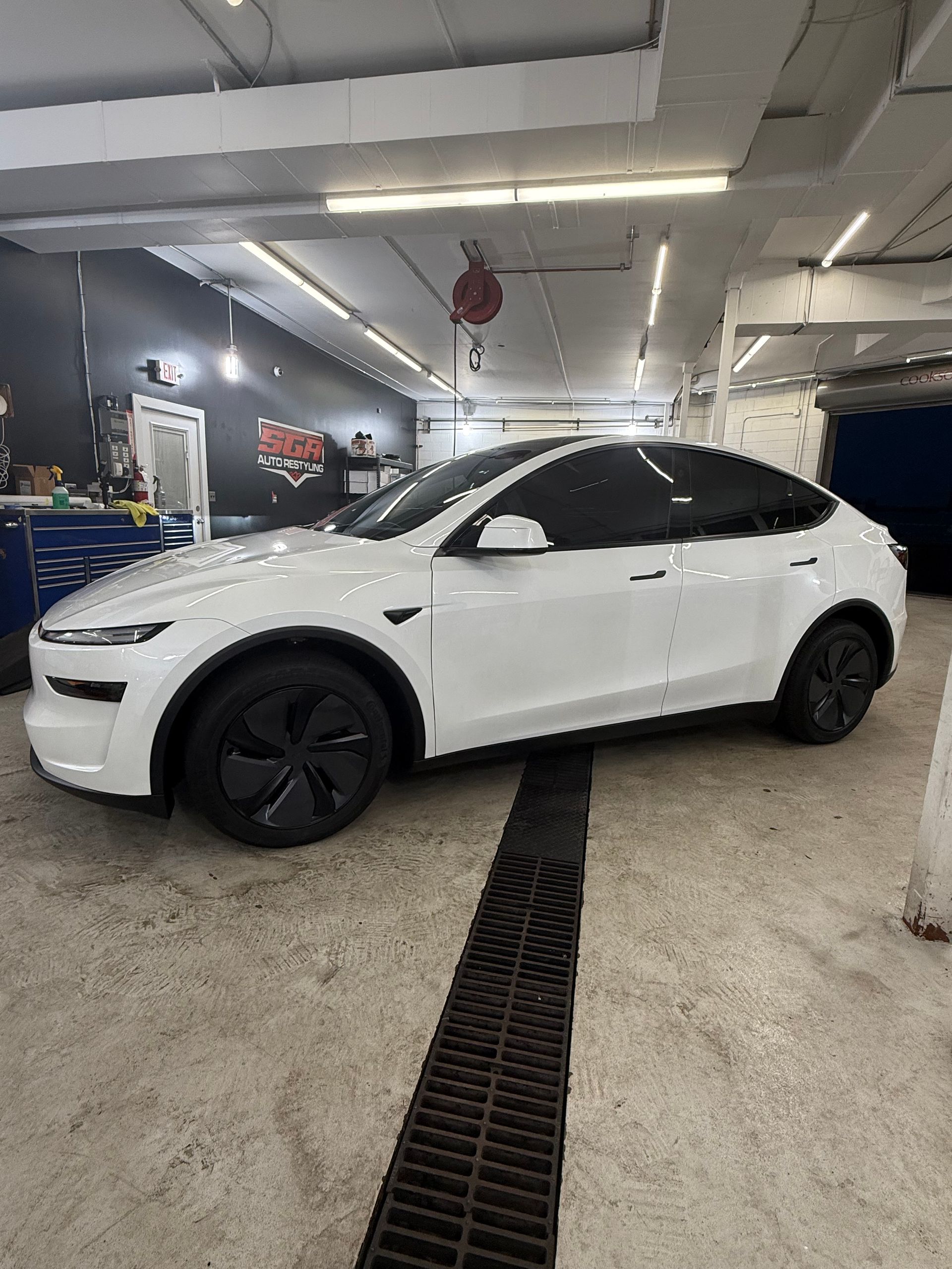 White Tesla Model Y with tinted windows inside a car detailing shop.
