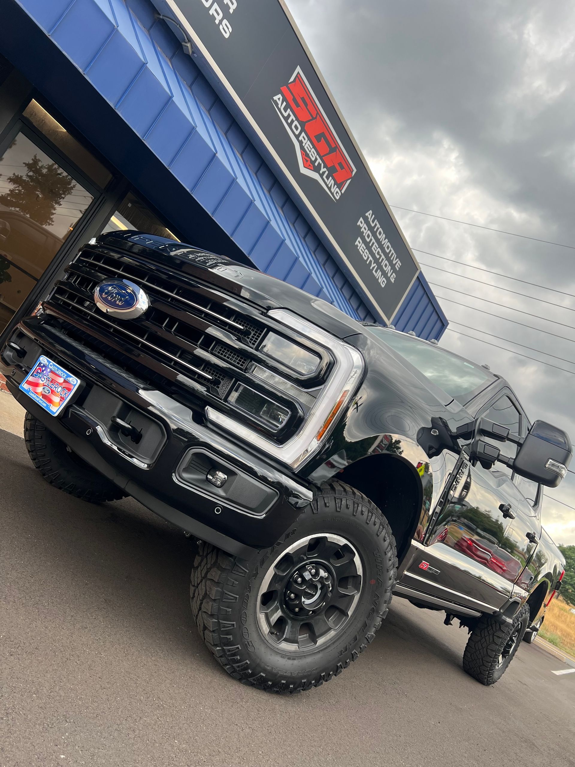 Black Ford pickup truck parked in front of a building with a business sign. Tires are off-road style.