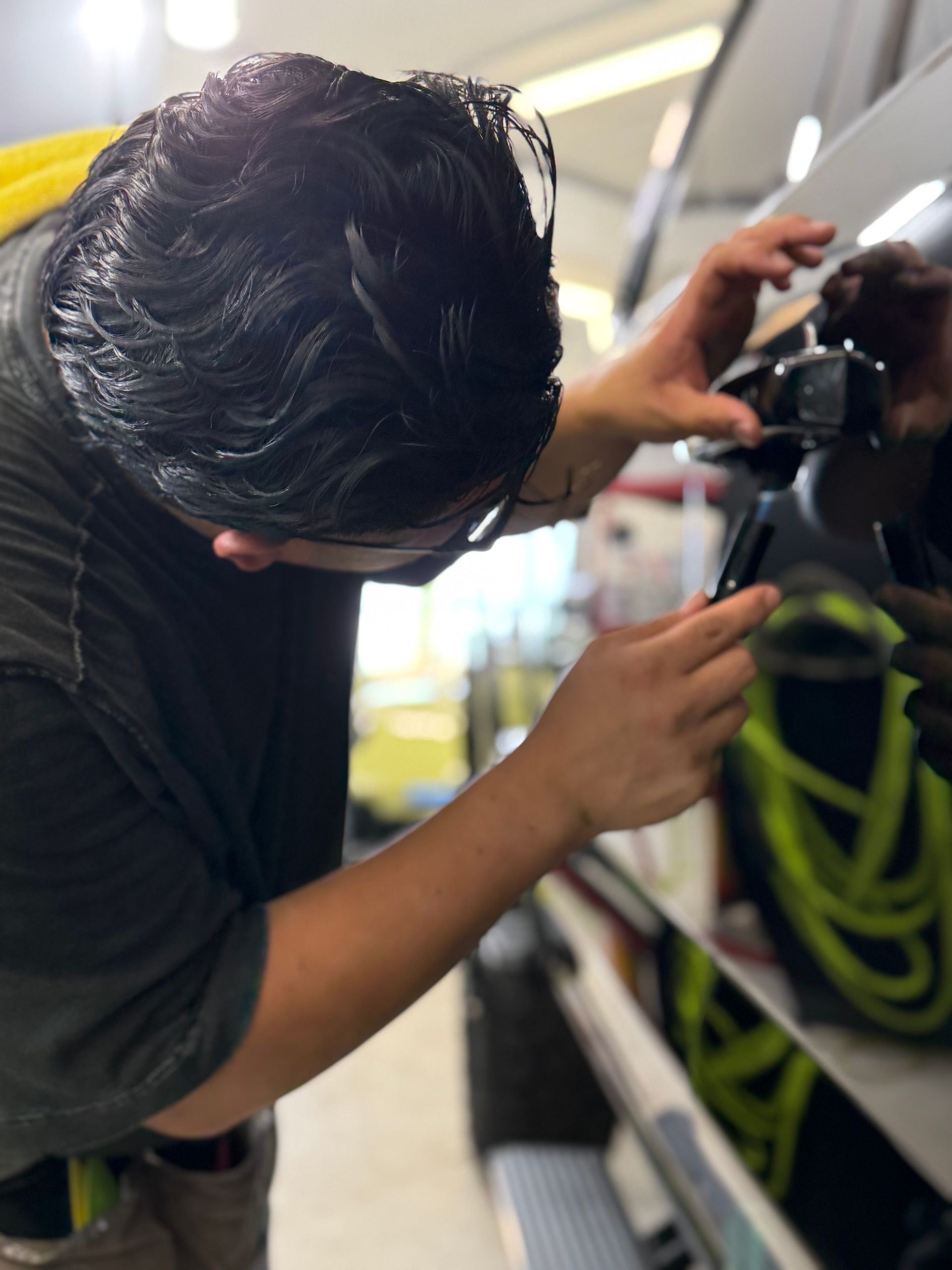 Person working on a black car door, using tools. The setting is likely a workshop or garage.