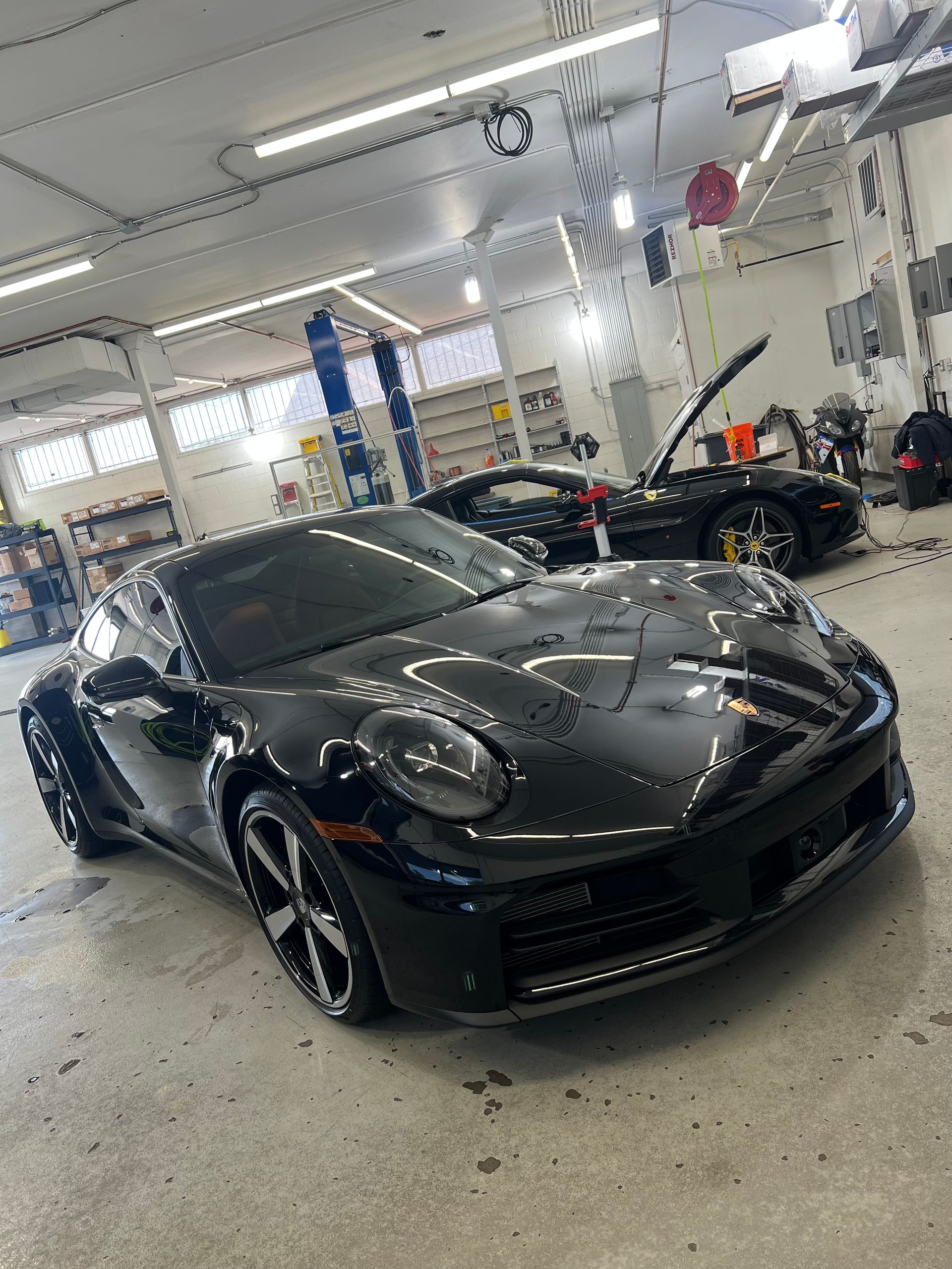 Black sports car in a garage with another car visible in the background.
