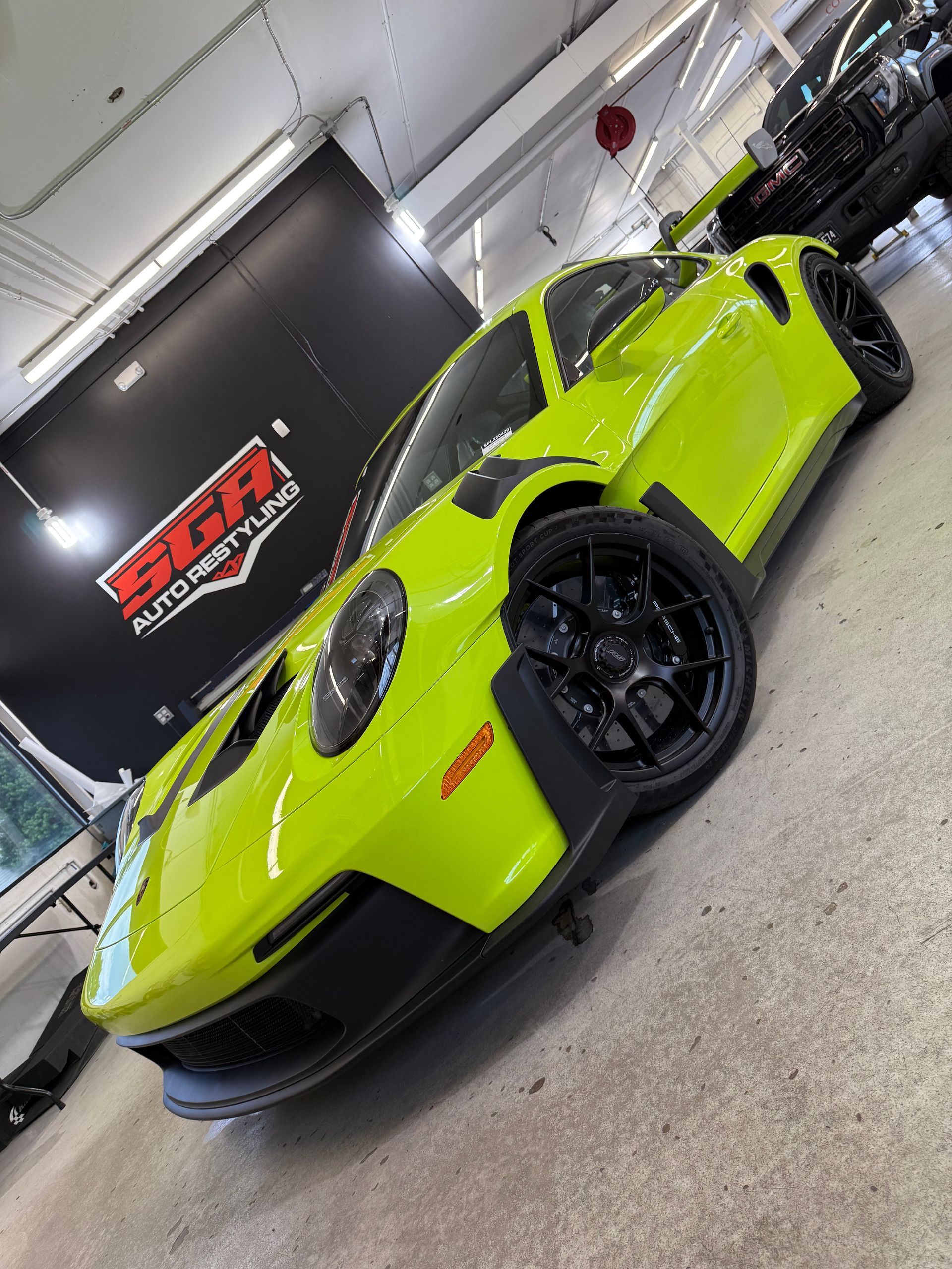 Green Porsche sports car with black wheels in a garage setting.